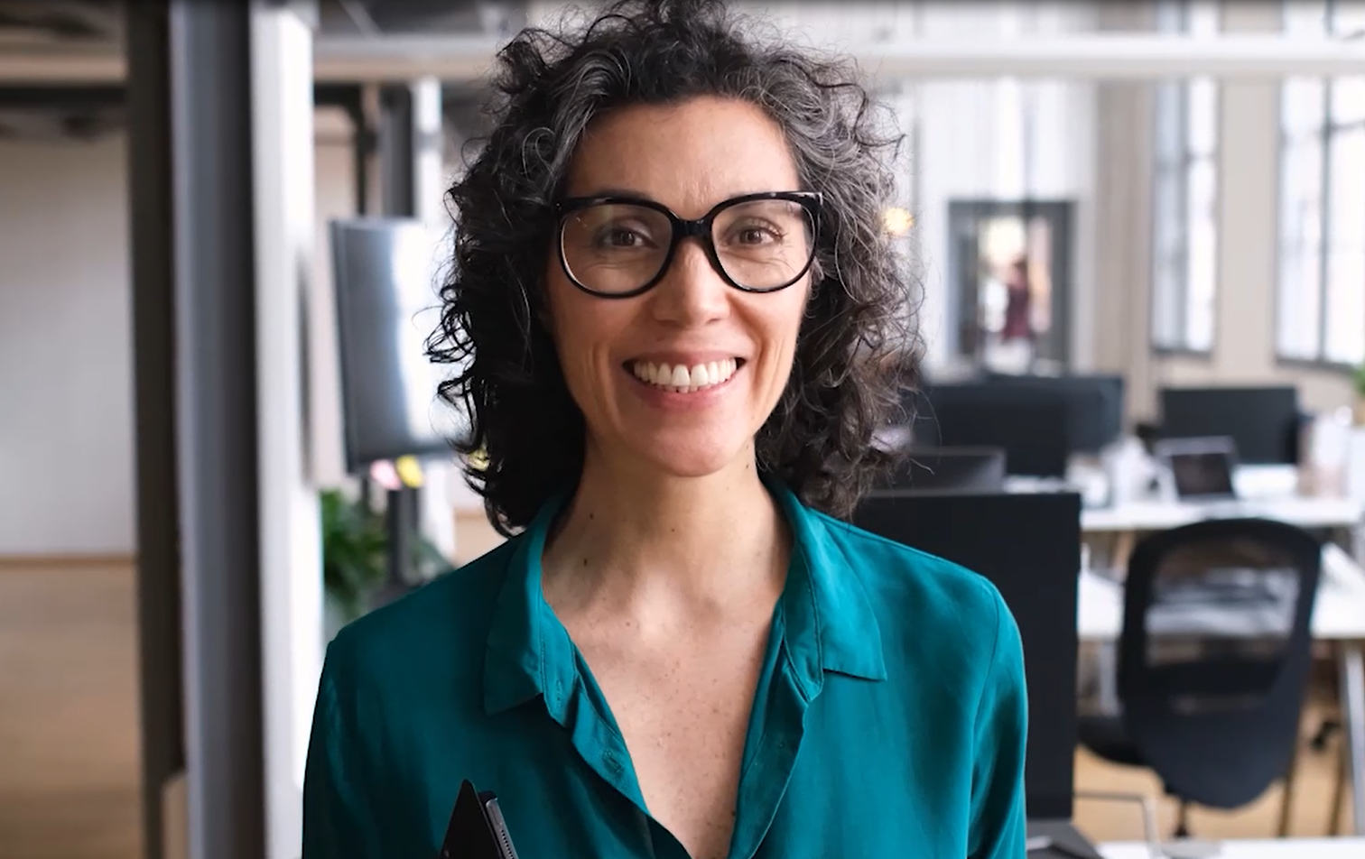 Eine Frau in einer Bluse steht in einem Büro und lächelt.