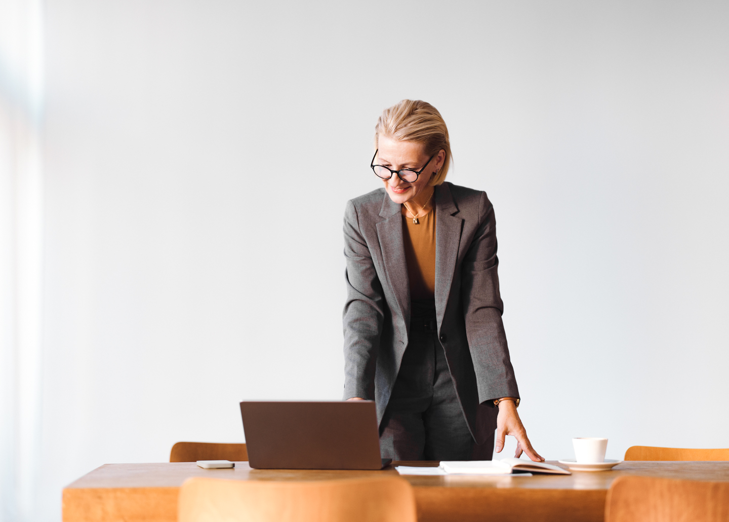 Eine ältere Frau stützt sich auf einen Tisch und blickt auf einen Laptop.