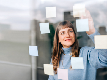 Eine junge Frau klebt lächelnd Post-its an ein Fenster.