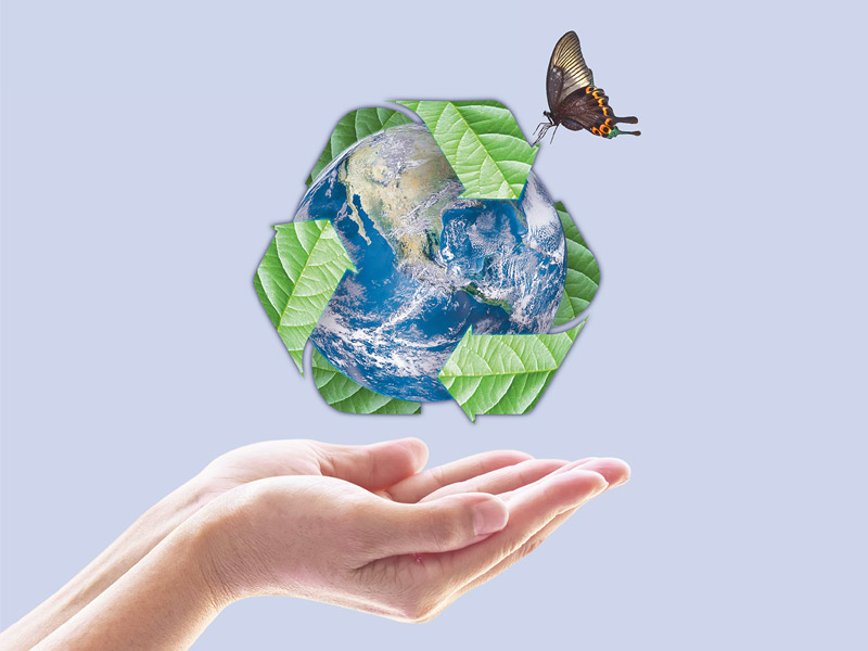 Über den Händen einer Person schwebt die graphische Darstellung der Erde umgeben von grünen Blättern in Form der Recycling-Pfeile auf denen ein Schmetterling sitzt.
